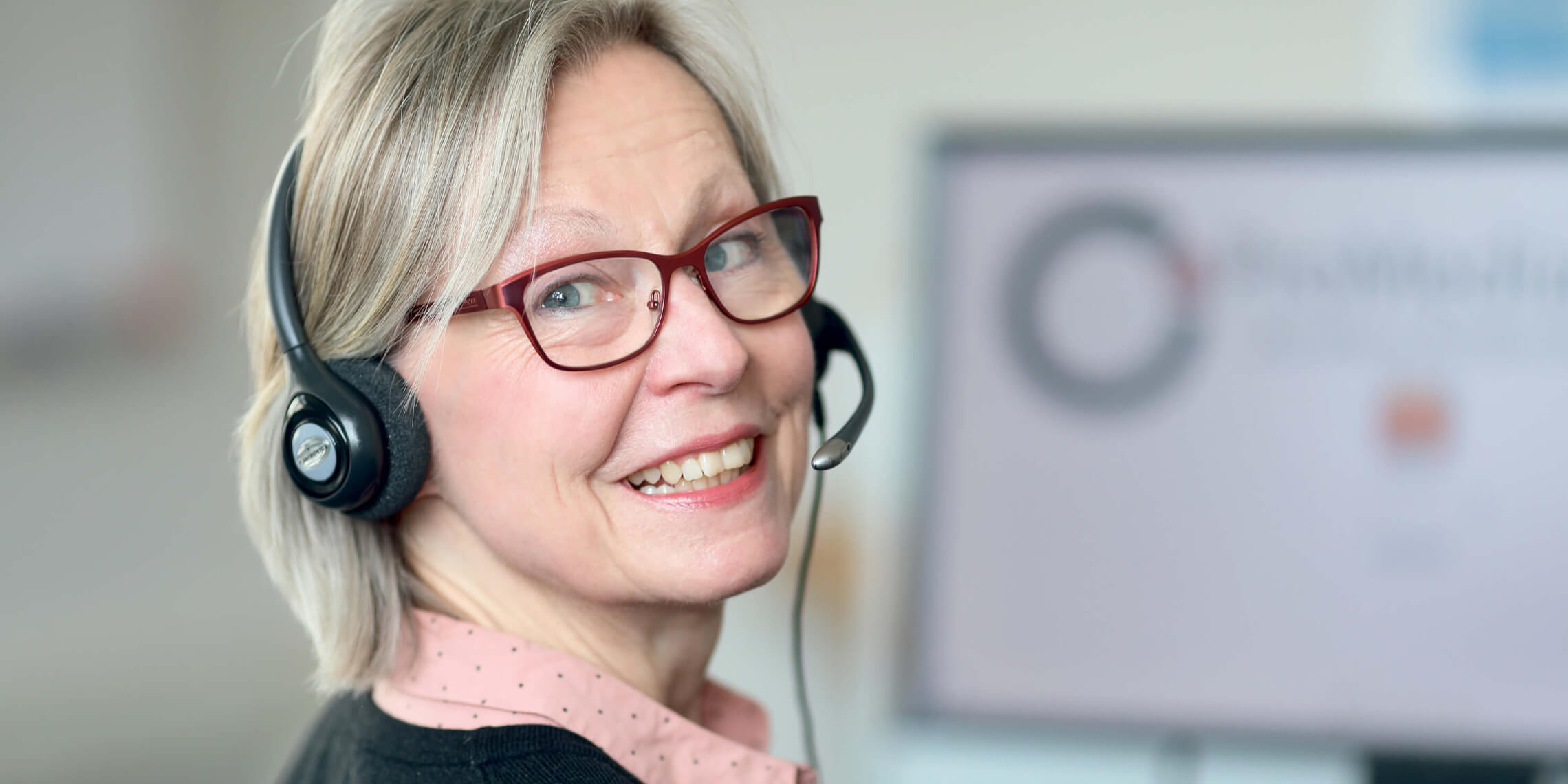 Pro Media Service Mitarbeiterin mit einem Headset im Büro vor einem Bildschirm